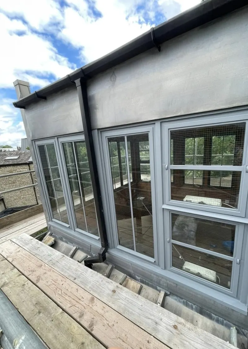 Restored timber casement windows painted pale grey on the Quaker Meeting House in Blackheath, seen from the scaffold
